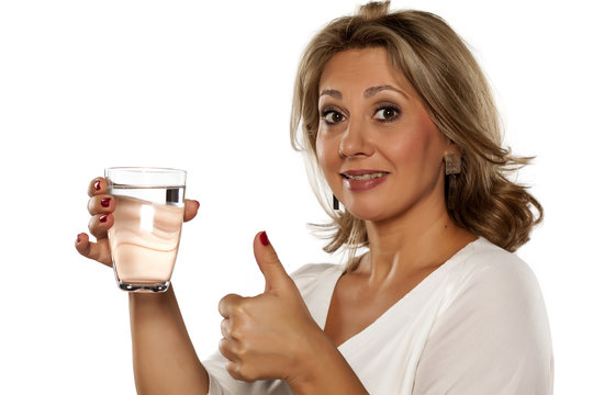 smiling middle-aged woman holding a glass with water and showing thumbs up
