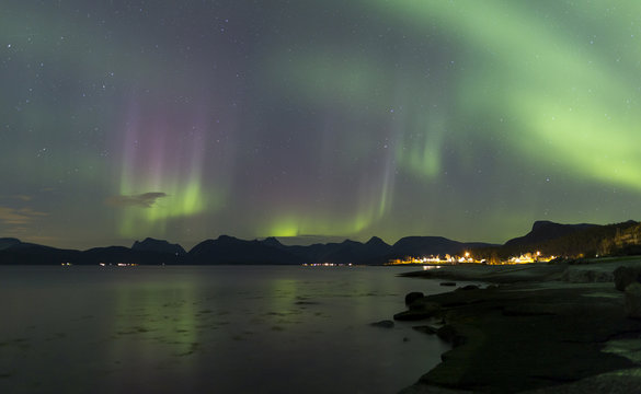 purple and green aurora over fjord with village lights