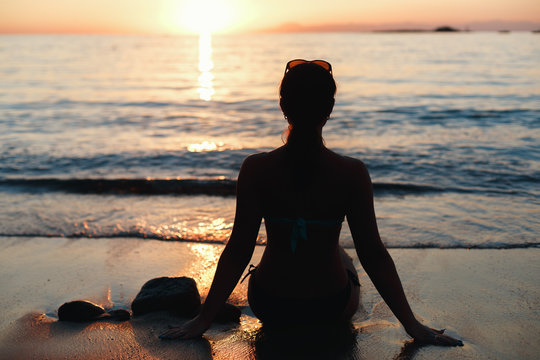 Girl On Shore Of Sea Sitting And Watching Sunset