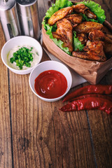 delicious grilled chicken wings with garlic and tomato sauce with lettuce in food paper bag on wooden rustic background top view, witi copyspace