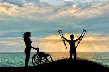Child disabled with crutches beside wheelchair and nurse on beach