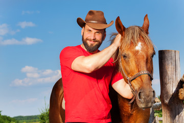 Portrait of smiling cowboy with his bay horse