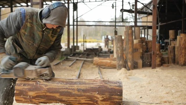 Construction worker planing a piece of wood for a building project. Construction grinds electric hand plane. Against the background of the factory premises, slow motion
