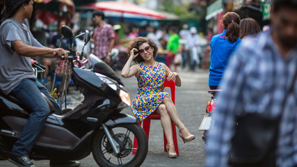 Young Asian woman sitting on a chair in the middle of a busy street.