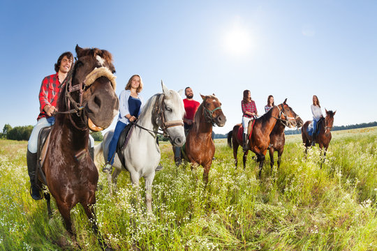 Happy equestrians riding horses in summer meadow