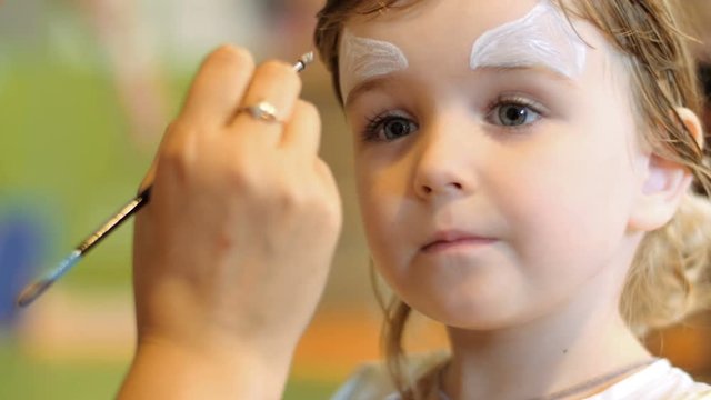 Little girl get painted face as a cat for a carnival