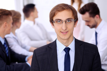 Portrait of cheerful smiling businessman  against a group of  people at meeting.