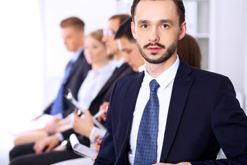 Portrait of cheerful smiling businessman  against a group of  people at meeting.