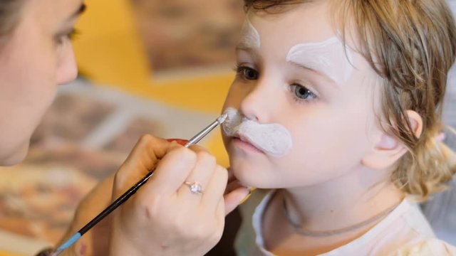 Little girl get painted face as a cat for a carnival