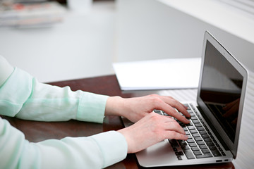 Business woman hands in a green blouse sitting at the desk in the office and typing on the laptop .