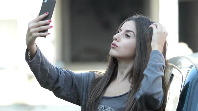 Young lady leaning on a car and taking selfies