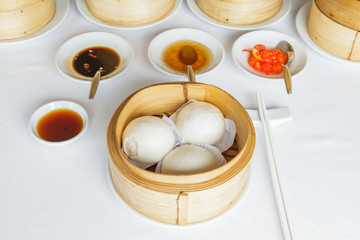 Fototapeta premium Dim sum food Steamed cream custard bun in bamboo basket at restaurant with soy sauce, sweet sauce, chili sauce and chopsticks.