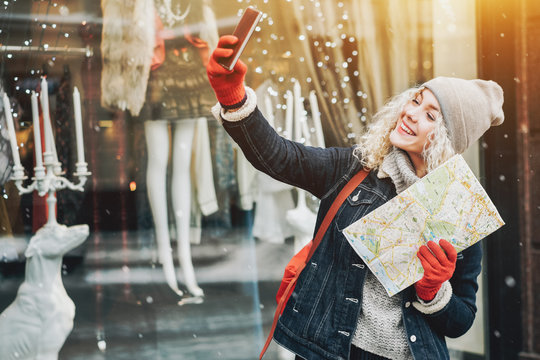 Smiling curly blond girl with map making selfie, winter