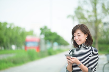 Obraz premium スマホを触るミドル女性・屋外