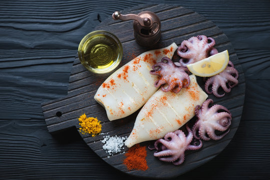 Black wooden serving board with cooked calamari and octopuses