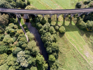 Aerial view of the railway bridge with shadow over path, river and green fields, New Mills, Derbyshire