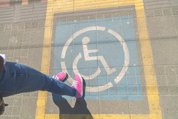 Handicapped person standing on a sign reserved for persons with disability. 
