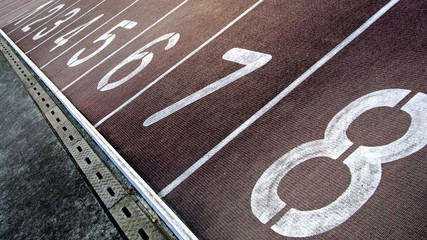 Running track with numbers from 1 to 8. Shot in a unique angle. A gutter along the track. Dark red and white colors. 