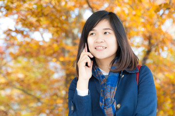 Happy young woman talking on mobile phone stand on autumn park