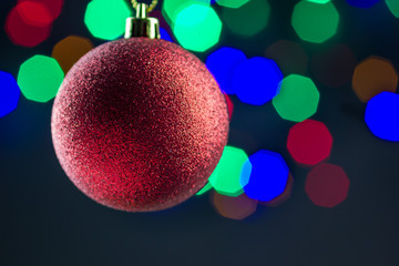 Red christmas ball hanging on gold ribbon with colorful bokeh background, copy space