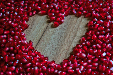 Pomegranate seeds with heart shape on a wooden table