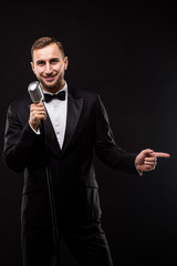 Young man in suit singing over the microphone with energy. Isolated on dark background. Singer concept.