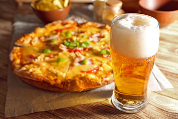 Glass of fresh beer and tasty pizza on background