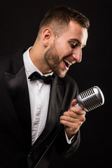 Naklejka premium Portrait of handsome man sing on microphone on black background. Singer concept.