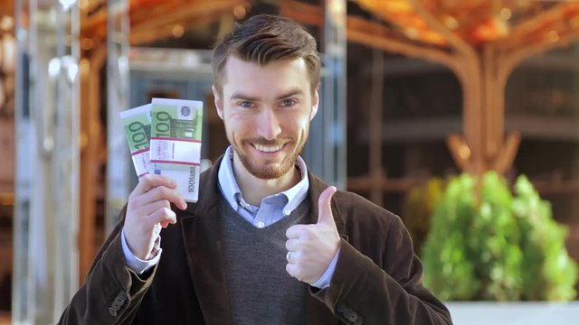 Happy man holding in his hand bundles of money cash Euro and showing thumbs up
