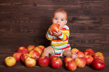 Adorable child with red apples on a wooden background

