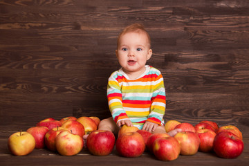 Fototapeta premium Adorable child with red apples on a wooden background