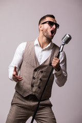 Naklejka premium portrait of young man in suit singing with the microphone. Isolated on grey background. Singer concept.