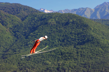 Professional skier flying from a ski jump on green mountains background at summer