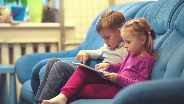 Little girl and teenage boy  With Digital Devices sitting on the sofa. Focus on boy.