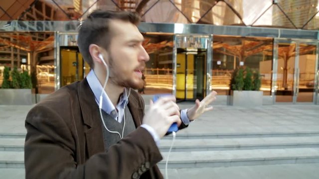 Handsome man listening to music in smartphone headphones, walking and dancing