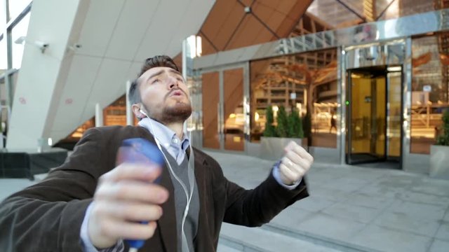 Handsome man listening to music in smartphone headphones, walking and dancing