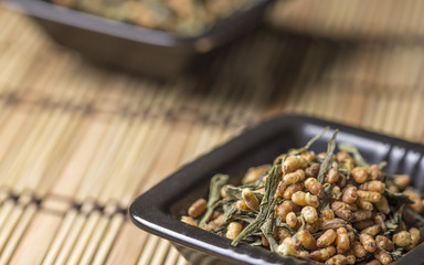 Genmaicha tea in black plate on bamboo tablecloth