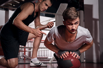 Man doing push-ups with trainer using fitness ball