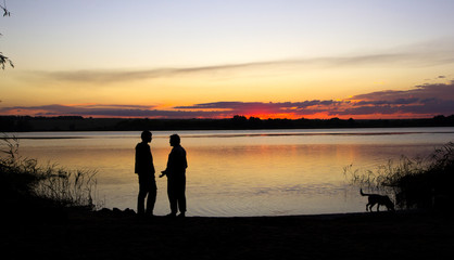 men and dog silhouette at sunset lake