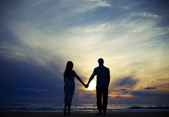 Romantic couple holding hands while looking to the sunset