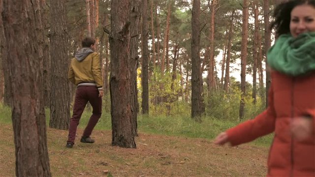 Girl flirts with guy and runs away from him in wood. Man with woman walks in forest. Young couple is spending time together. Best moments of life