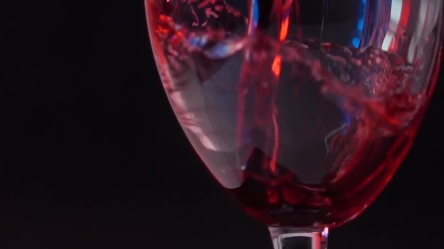 Pouring red wine into glass against black background with French flag-like highlight. Winemaking and travel to France concepts. Super slow motion shot