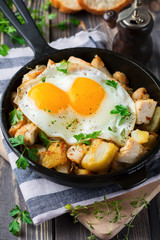 Hearty breakfast. Hash brown potatoes, chicken, onion, parsley, oregano and a fried egg in a frying pan on the old wooden background. Selective focus.