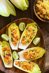 Chicoree Blätter belegt mit einem Salat aus Couscous, Kürbis, rote Zwiebel und Thymian serviert mit Limonenstücken auf Holzteller, fotografiert mit natürlichem Licht 