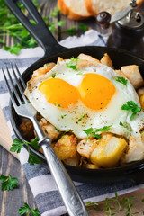 Hearty breakfast. Hash brown potatoes, chicken, onion, parsley, oregano and a fried egg in a frying pan on the old wooden background. Selective focus.