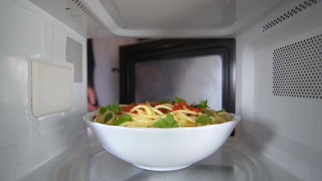 Man wearing a robe heating up cooked pasta dish with tomato sauce in the microwave oven at residential kitchen view inside the microwave