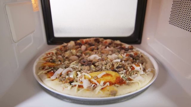 Frozen seafood pizza Frutti di Mare in microwave oven. Mussels, shrimp, clams, calamari, olives, tuna pizza topping. Inside view version with external lighting.