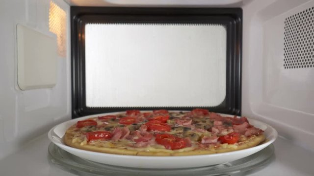 Baked mushroom ham pizza heating in microwave oven inside view