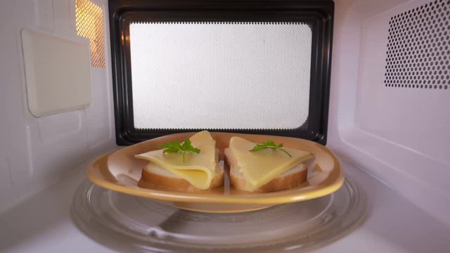 Making toasts with melted cheese. Process of melting cheese slices on bread in the microwave oven inside view.