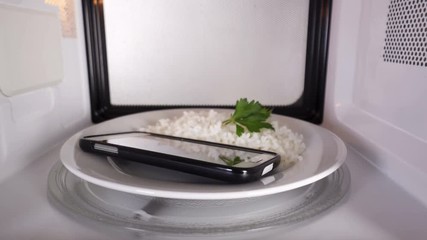 Cell phone with rice on a plate heating in the microwave oven inside view